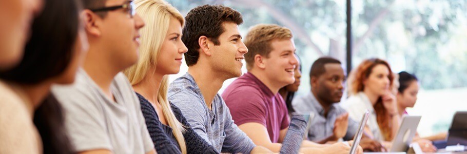 A group of students happily watching a lecture with their laptops open in front of them.