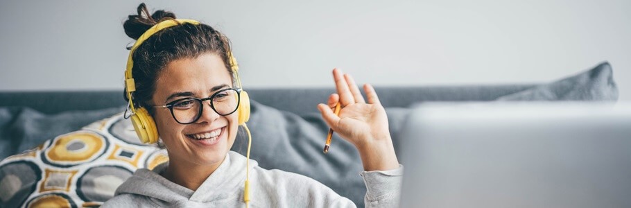 A student waving at a laptop whilst wearing headphones.